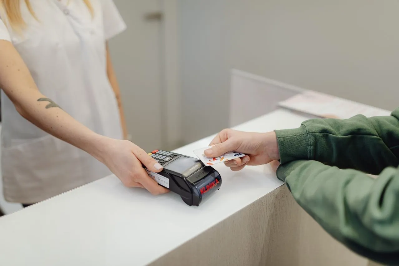 Au comptoir, une commerçante tient un terminal de paiement et un client règle par carte bancaire